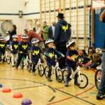 A teacher gathers a line of young students in a school gym who are are bikes