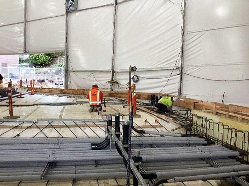 under a large tent, 白色防水材料有一堆电线导管放置在一个guie框架与钢筋下面